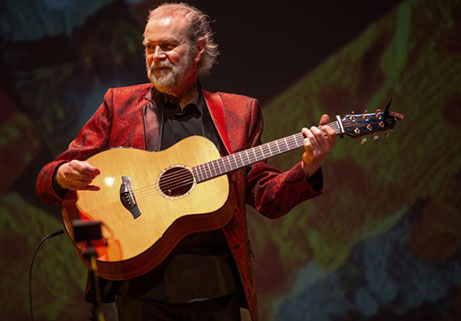 Beppe Gambetta performing live acoustic guitar on stage in a red jacket at Locktown Stone Church concert.